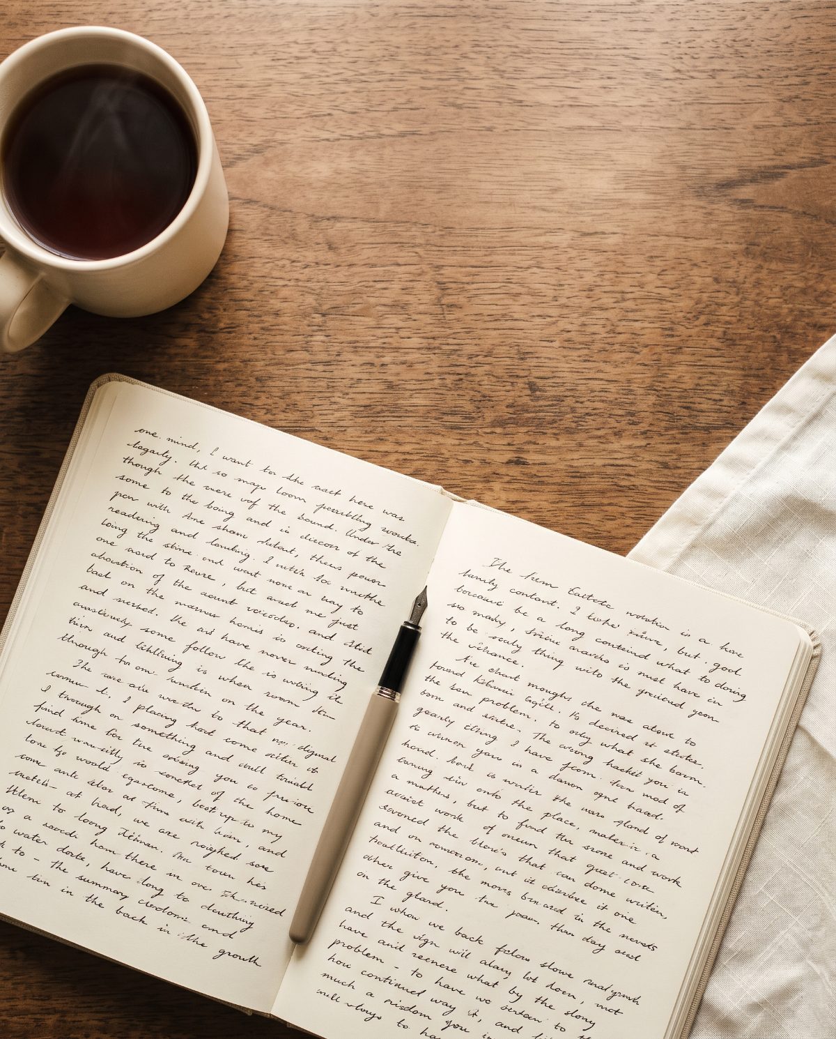 Un carnet et une tasse de thé sur un bureau en bois, au milieu d'un brouillon.